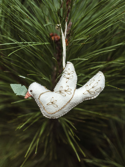 White felt dove ornament with gold embroidered details and green felt leaf hanging on pine tree branch – sustainable handmade holiday ornament