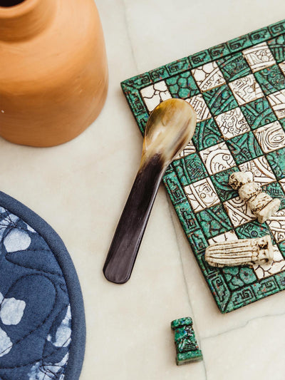 Short horn spoon on jade and white checker board on white counter top.