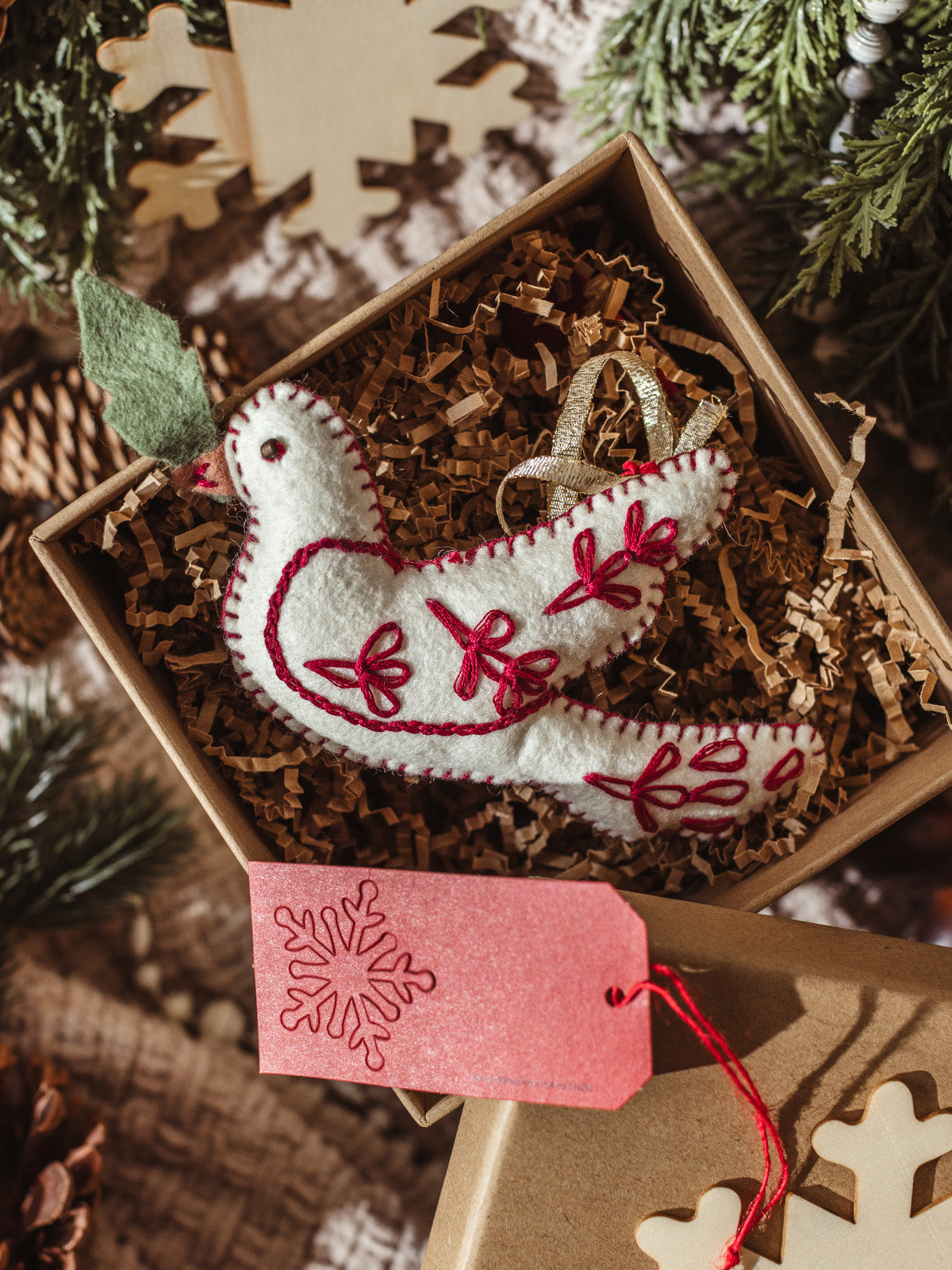 Handmade red-stitched felt dove ornament packaged in eco-friendly holiday gift box with crinkle paper and festive gift tag