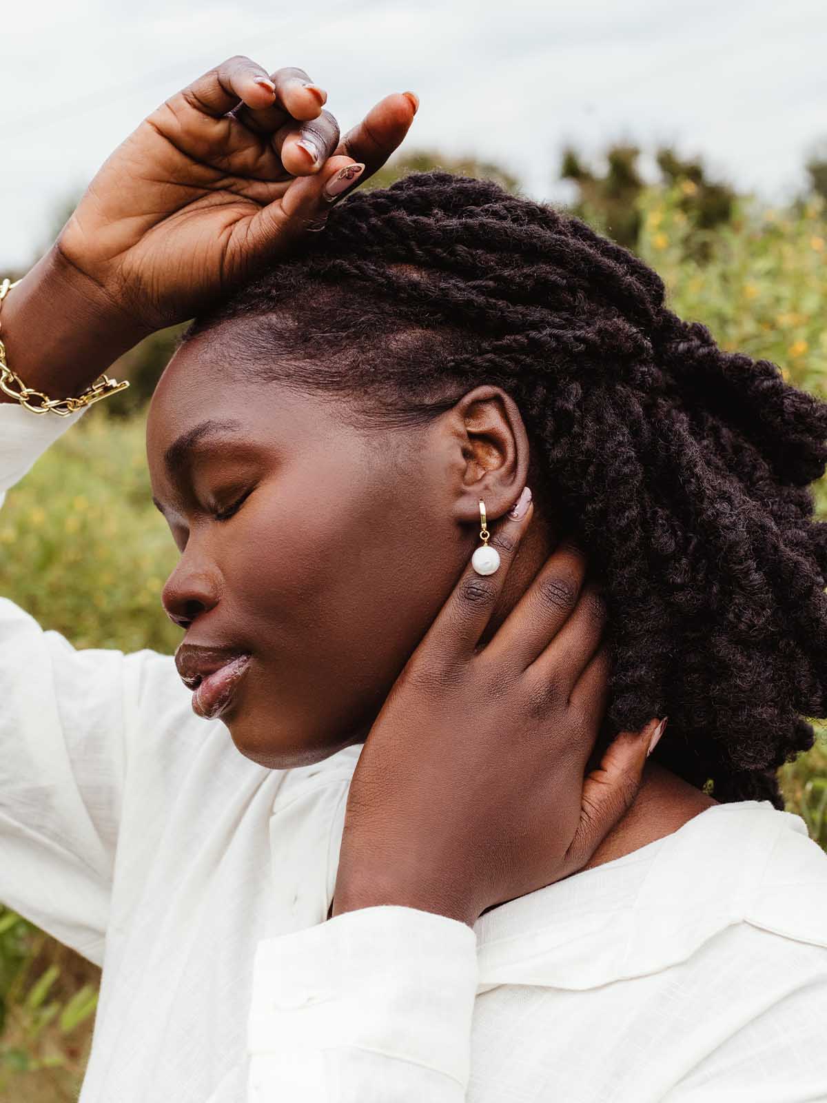 Woman with braided hair posing with gold hoop pearl drop earrings and gold jewelry, highlighting ethical fashion accessories.