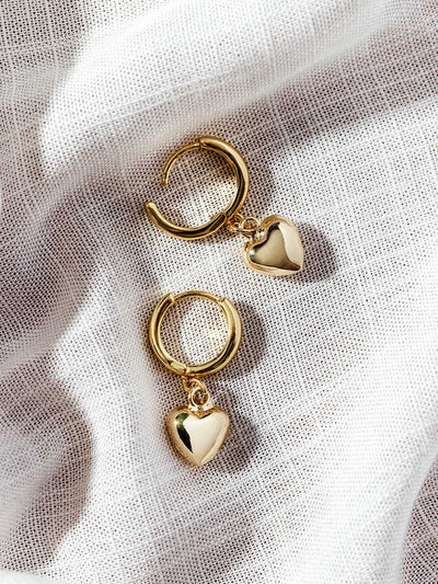 Gold heart charm hoop earrings on white fabric background – dainty sustainable jewelry perfect for everyday wear or gifting.