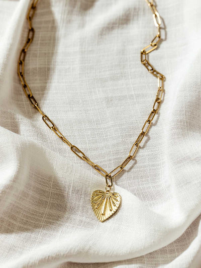 Close-up of gold paperclip chain necklace with detailed heart pendant, laid on soft fabric – minimalist ethical jewelry for women.
