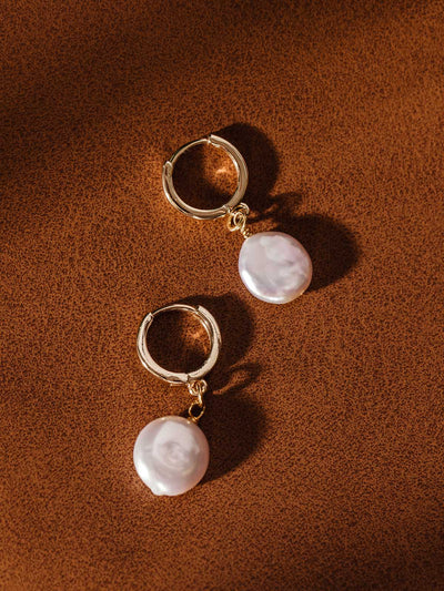 Gold hoop earrings with white freshwater pearl charms on warm brown background – timeless ethical jewelry with natural pearls.