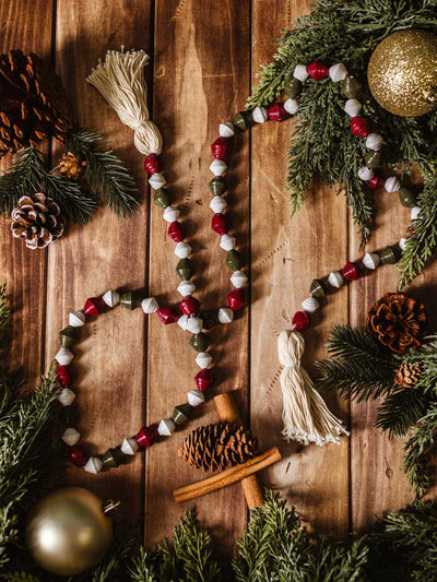 Handmade Christmas garland with red, green, and white paper beads and tassels, displayed with pinecones, cinnamon sticks, and festive greenery.