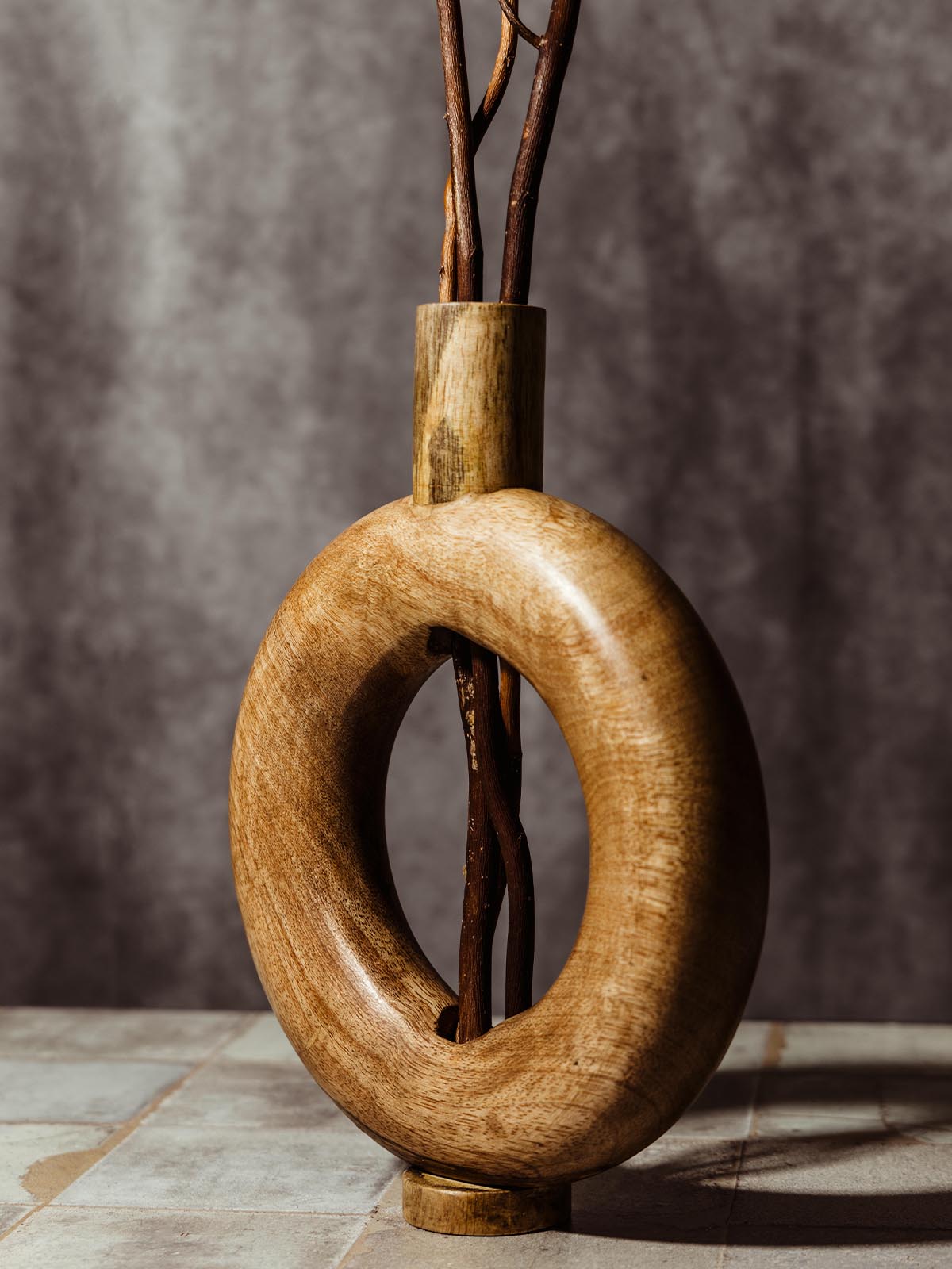 Handcrafted wooden vase with a modern circular design, featuring natural wood grain and branches arranged through the center. This ethically made home decor piece adds a rustic and elegant touch to any space, highlighting sustainable craftsmanship.