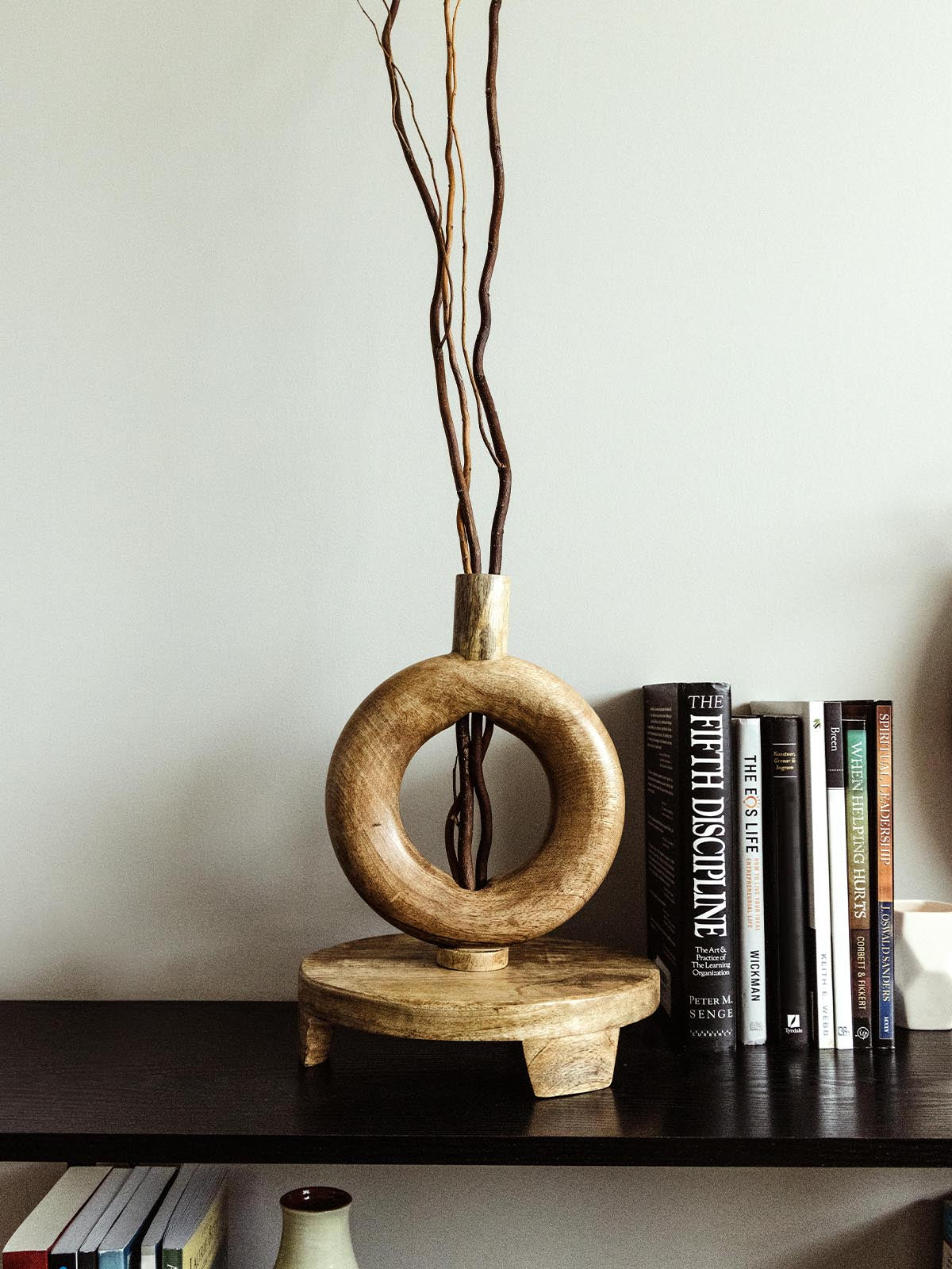 Handcrafted wooden sculpture with circular design and tall, decorative branches displayed on a modern shelf, accompanied by books. Ethically made home decor piece from Joffa.
