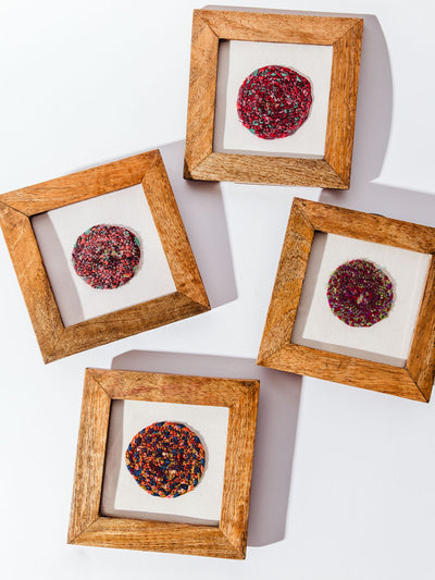 Four framed circular textile art pieces with vibrant red, pink, and multicolored patterns, each displayed in a natural wood shadow box frame on a white background.