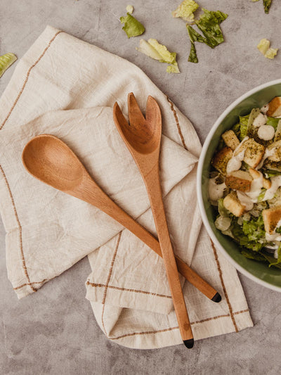 Set of wood serving spoons on counter with napkin and salad dish.