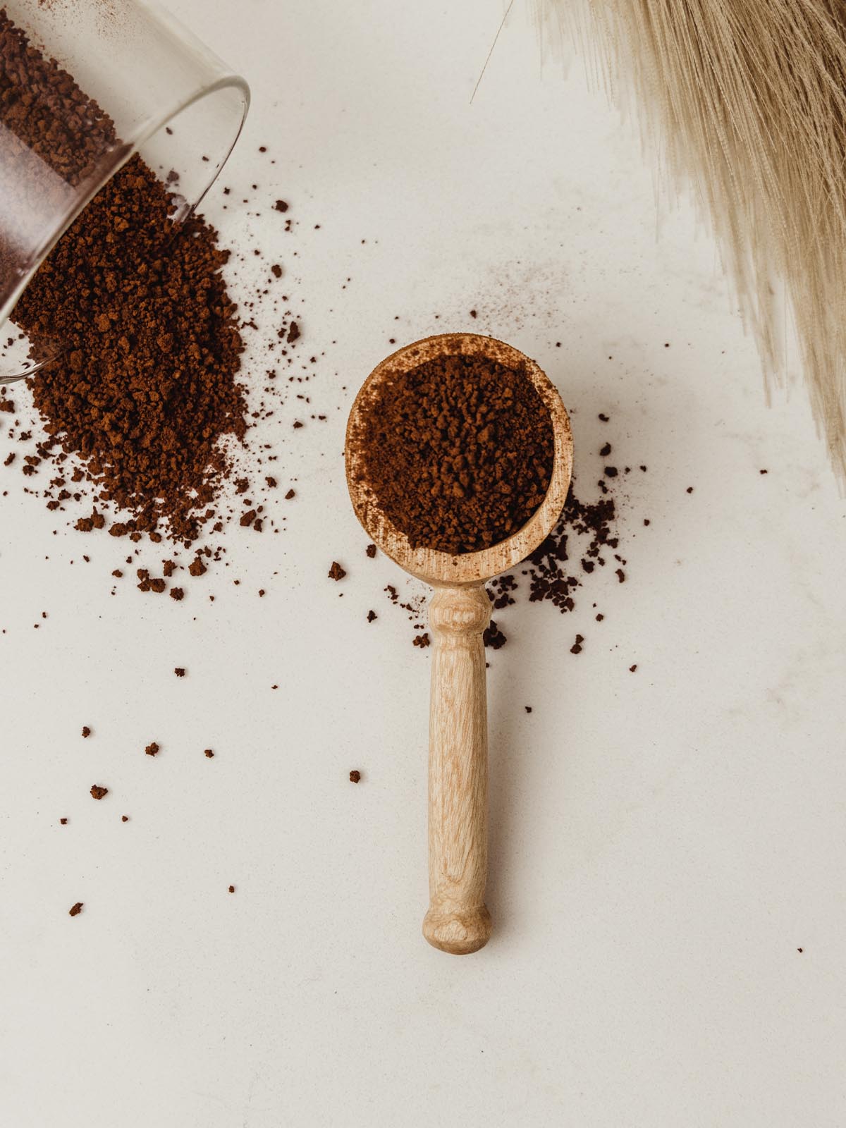 Coffee scoop on white counter with coffee grounds in scoop and spilt on counter.