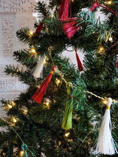 Red, green, and white tassel garland hanging on holiday tree.