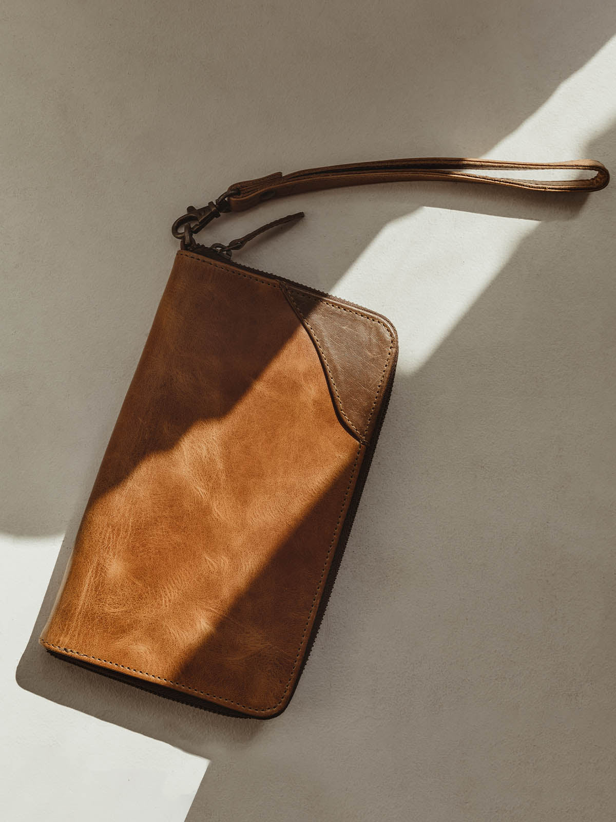 Closed Rani Wallet on white table with dark brown leather detail on the corner of the wallet. Wristlet on the end of the rani wallet. 