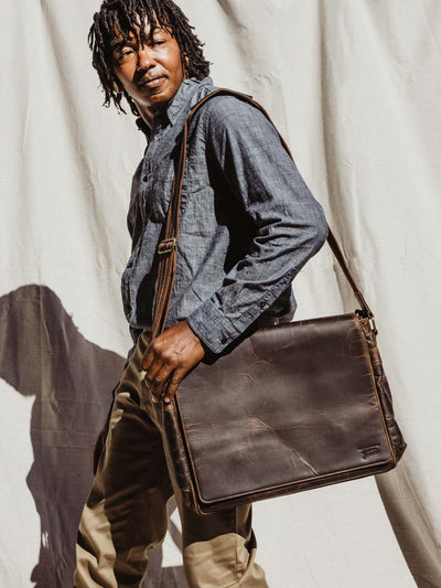 Male model in business casual clothing holding travel bag over the shoulder.