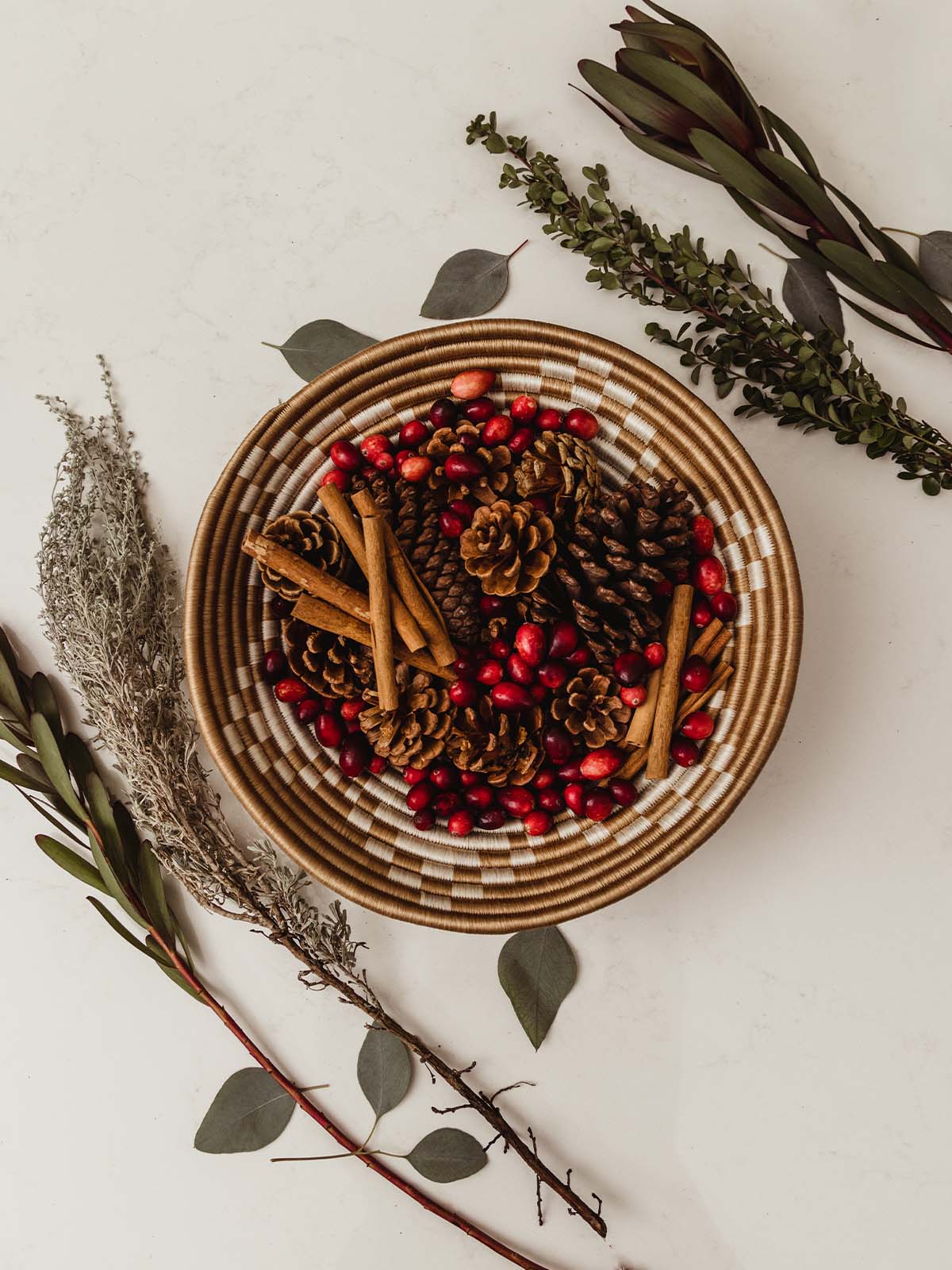 Large woven bowl containing poperi with greenery surrounding the bowl on a white counter surface.