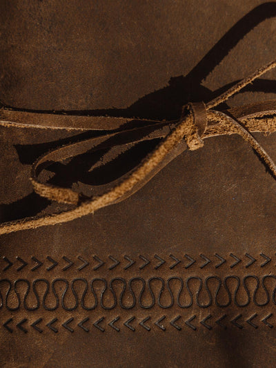 Details of buffalo leather carving. Has a wave like pattern with arrows above and below the wave pattern. Journal is tied closed with leather string.