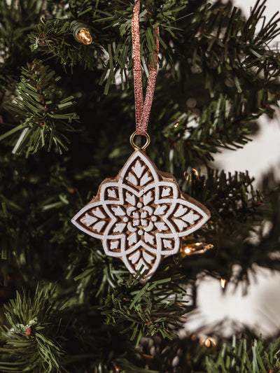 Wooden star carved with white details and silk string to hand on a holiday tree. 