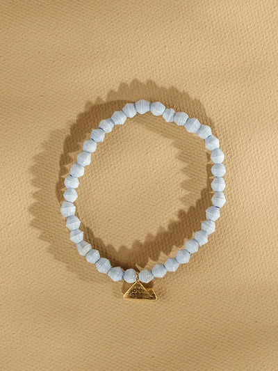 Pale blue beaded bracelet with golden mountain charm. Bracelet is placed on a tan background.