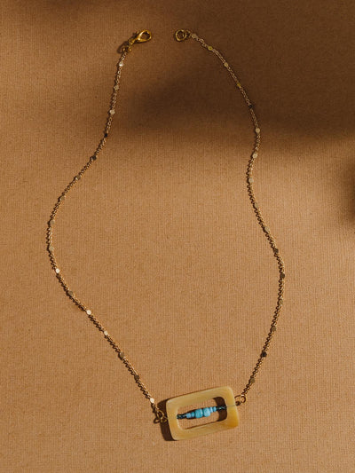 golden chain with details in the chain. Rectangulat pendant with turquoise beads in the middle of the rectangle shape. 