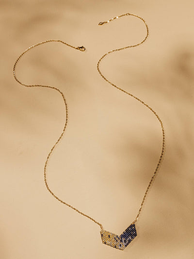 Blue and gold pendant on a long gold chain on a tan background.