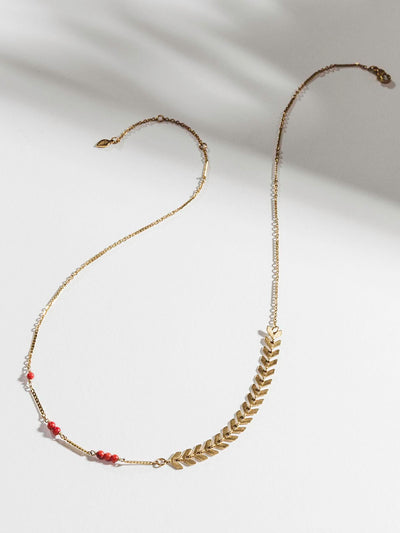 Golden chain necklace with arrow shapes and red beads on white background.
