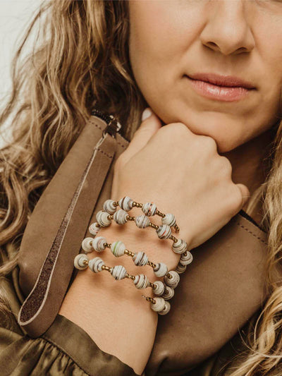 Wrap bracelet with golden and white beading on a female model holding a wristlet purse.