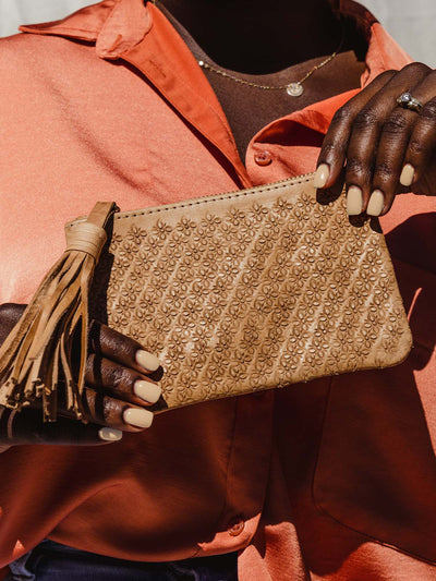 Model holding light tan leather pouch with tassel and carved floral pattern