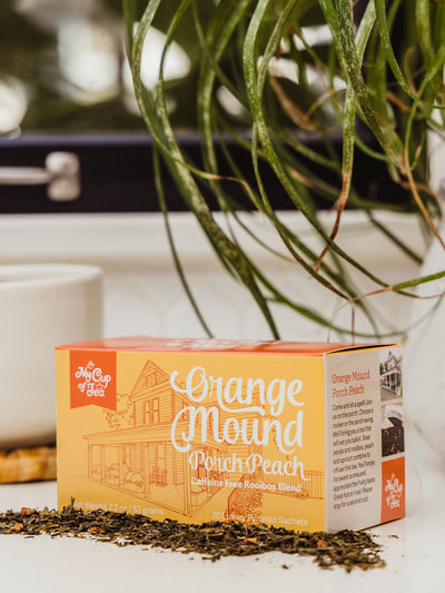 Peach Tea box on counter with coffee cup and greenery.