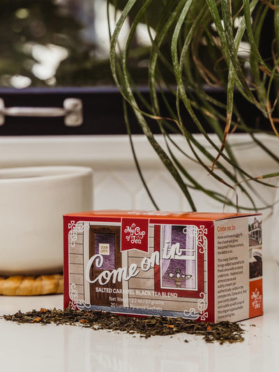 Salted Carmel Black Tea box on counter with coffee cup and greenery.