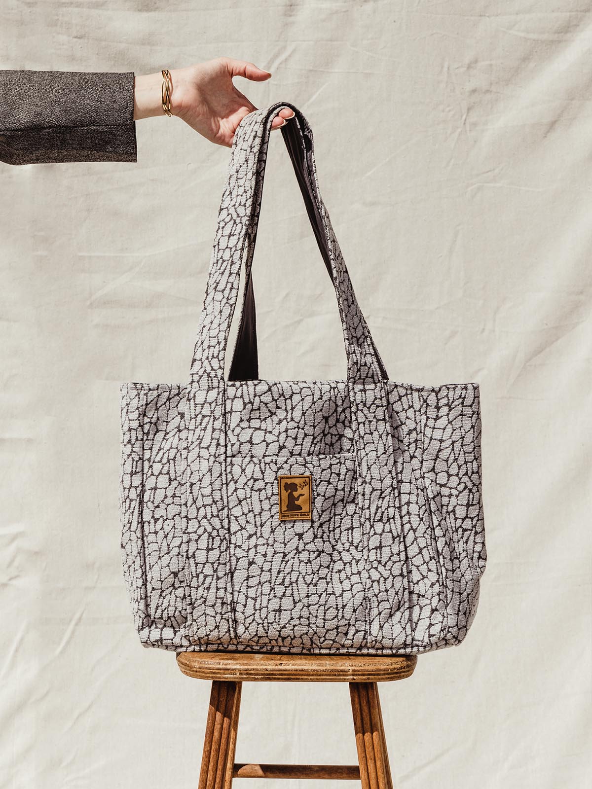 Model holding grey textured tote bag on stool on cream backdrop