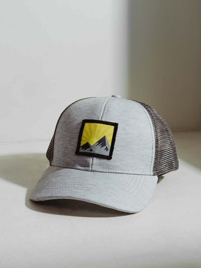 Mens light grey hat with mountain scene patch and netted back on white table.