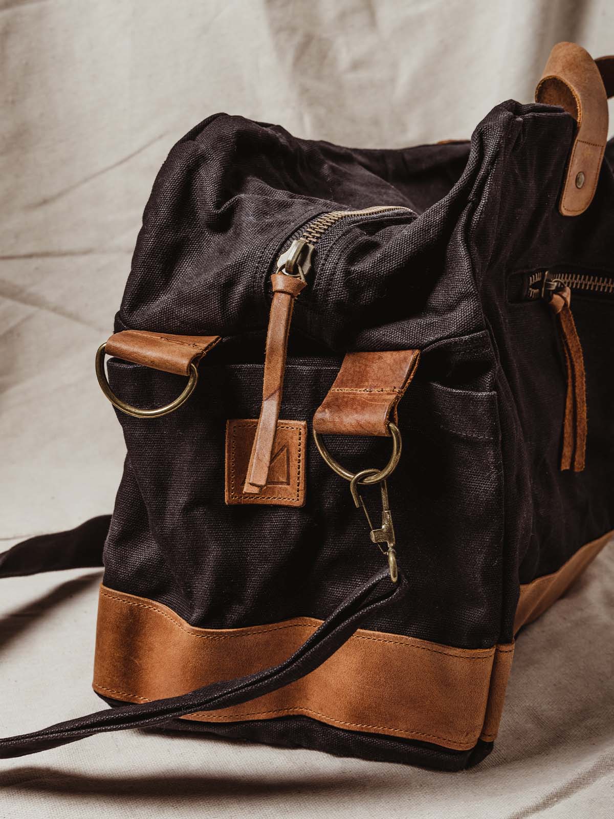 Details of black weekender bag with leather details, strap clips, and bags main zipper.