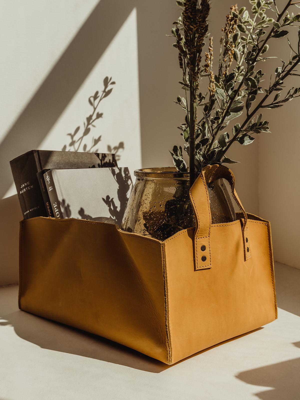 Carmel colored leather storage bin with books, glass vase, and floral arrangement