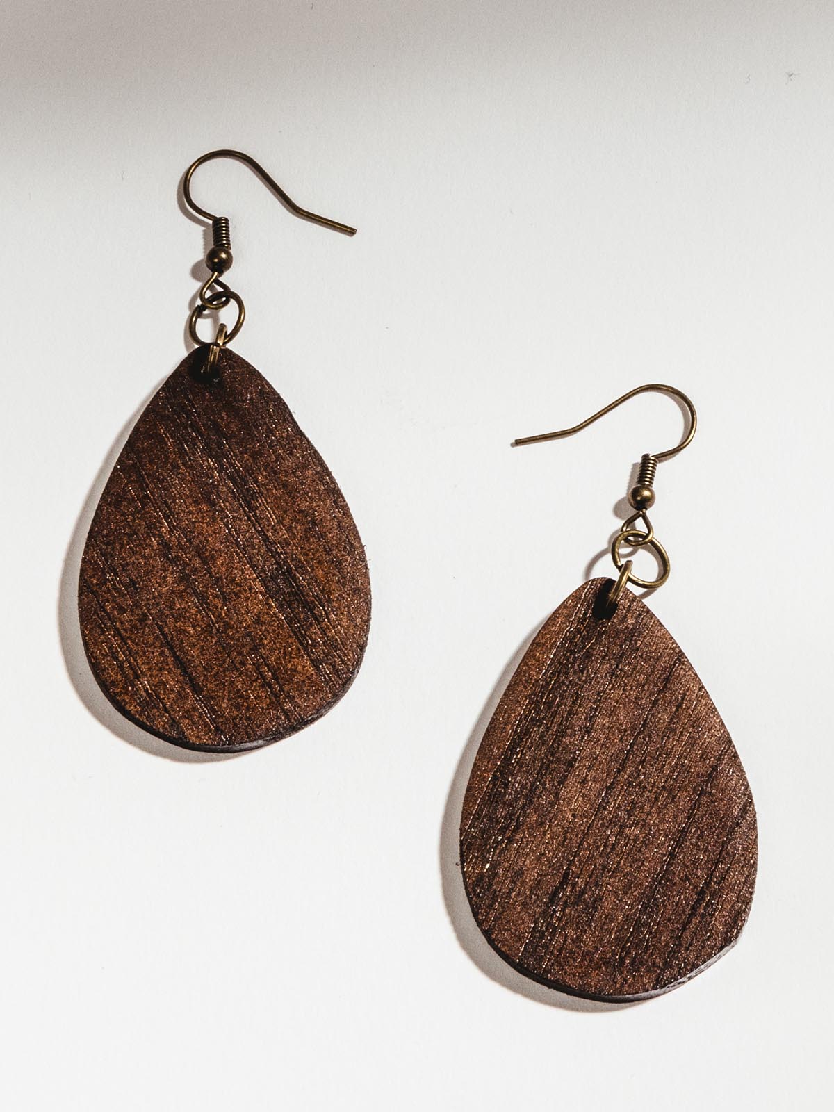 Dark brown wooden tear drop earrings on white table.