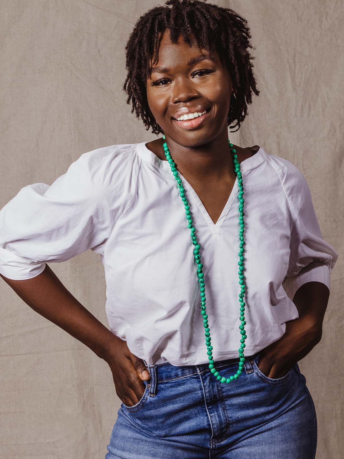 Turquoise necklace worn long on a model wearing a white blouse.