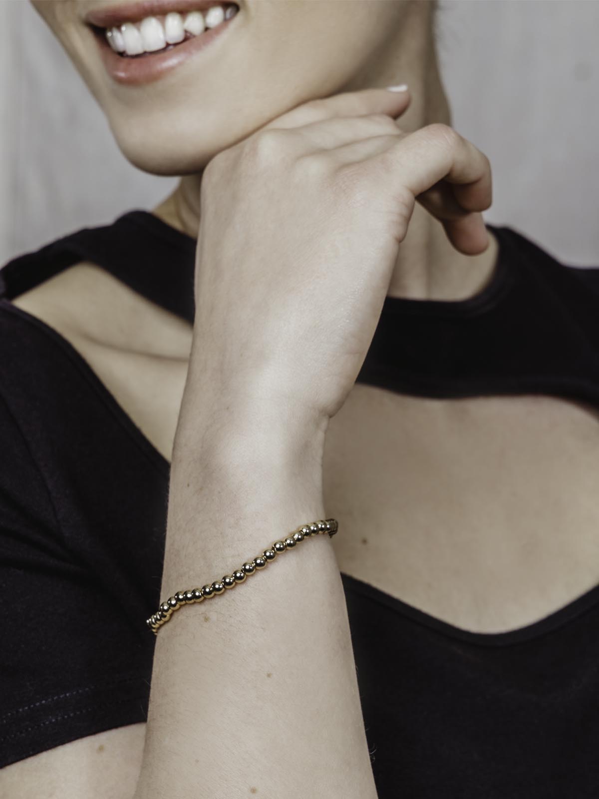 Smiling woman with black dress wearing gold beaded bracelet