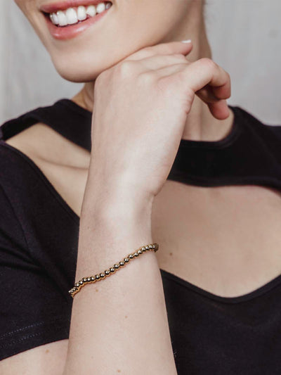 Smiling woman with black dress wearing gold beaded bracelet