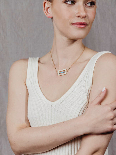 model wearing golden chain with details in the chain. Rectangulat pendant with turquoise beads in the middle of the rectangle shape. 