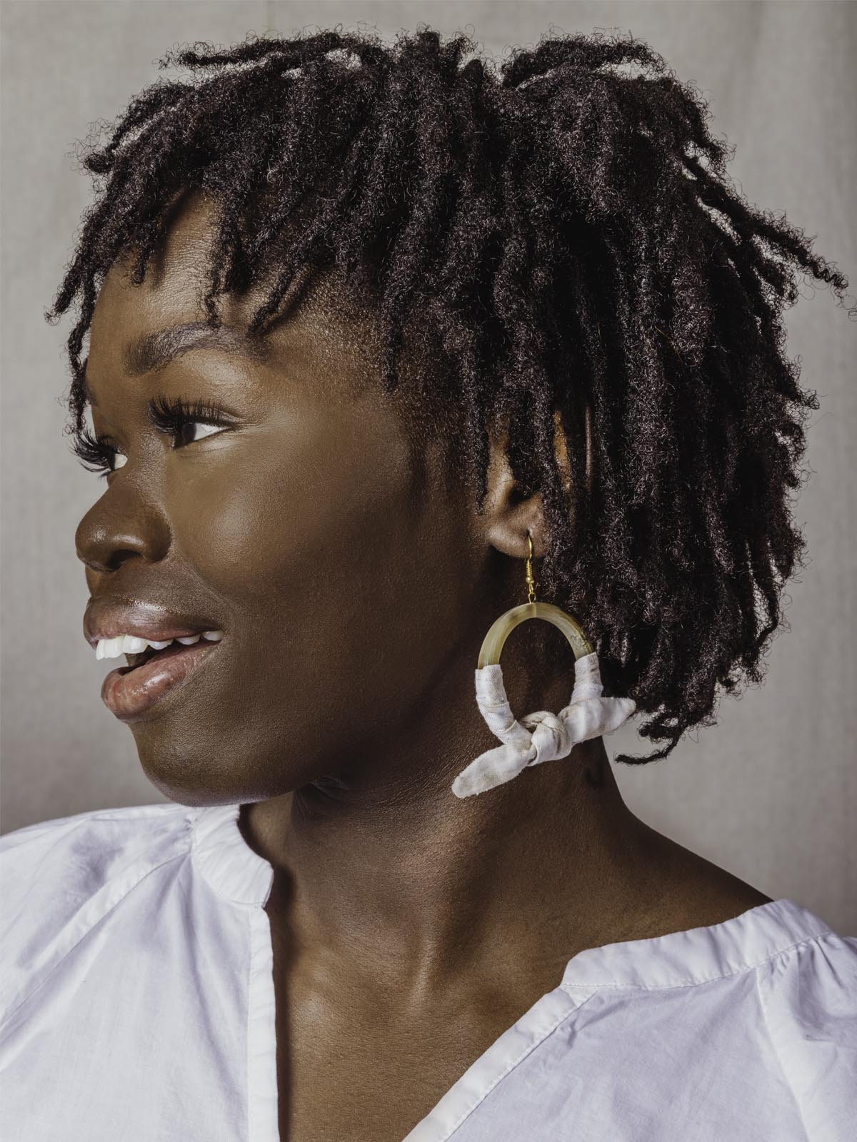 Model wearing horn hoop earring with canvas-like cloth wrapped around and tied in a bow.