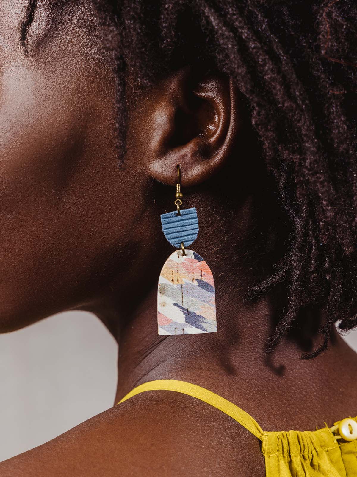 Colorful bright half circle earrings with blue upside down half circle with gold hardware on model wearing yellow top. 