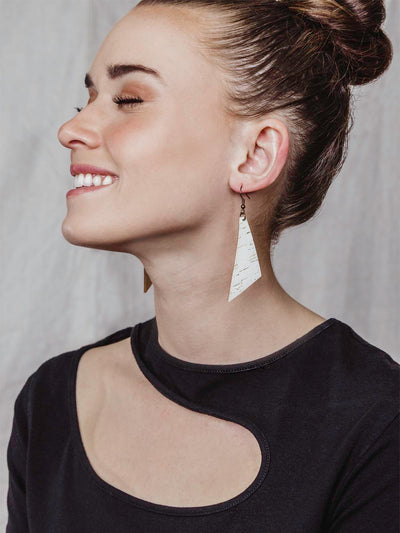 Women wearing a black top with white cork earrings in the triangular shape on her ears. 
