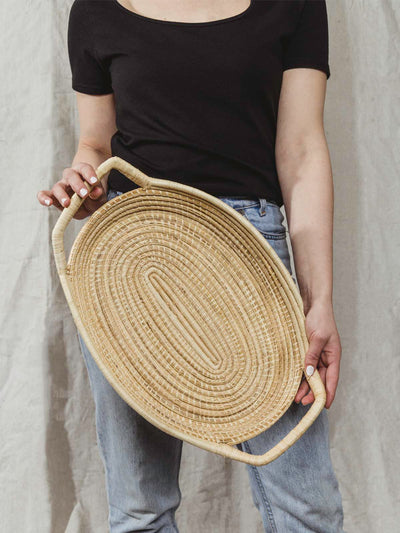 model holding large woven serving tray in a light tan color