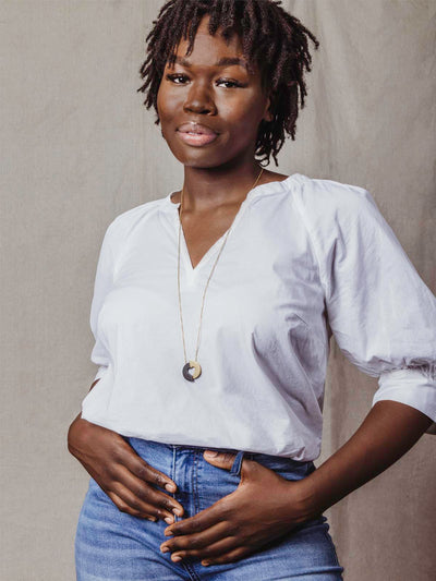 Model wearing white top with jeans and two toned heart necklace. 