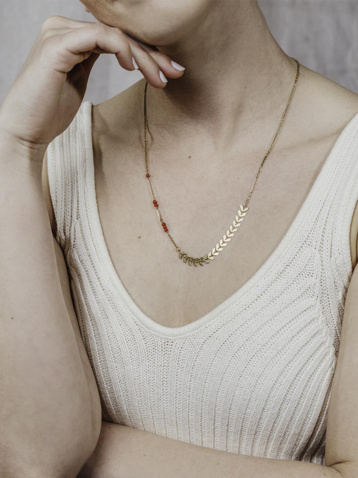 Model wearing golden chain necklace with arrow shapes and red beads