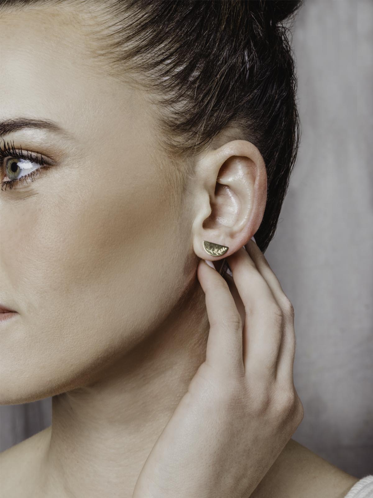 Model wearing half moon shaped golden studs on white surface with mustard seeds etched into the gold.