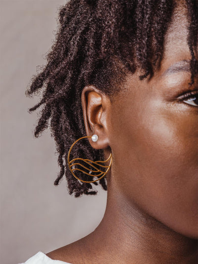 Model wearing golden hoops with water-like design inside the hoop complete with pearl stud