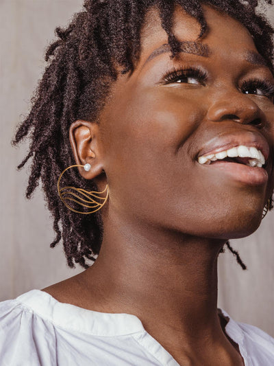 Model wearing golden hoops with water-like design inside the hoop complete with pearl stud