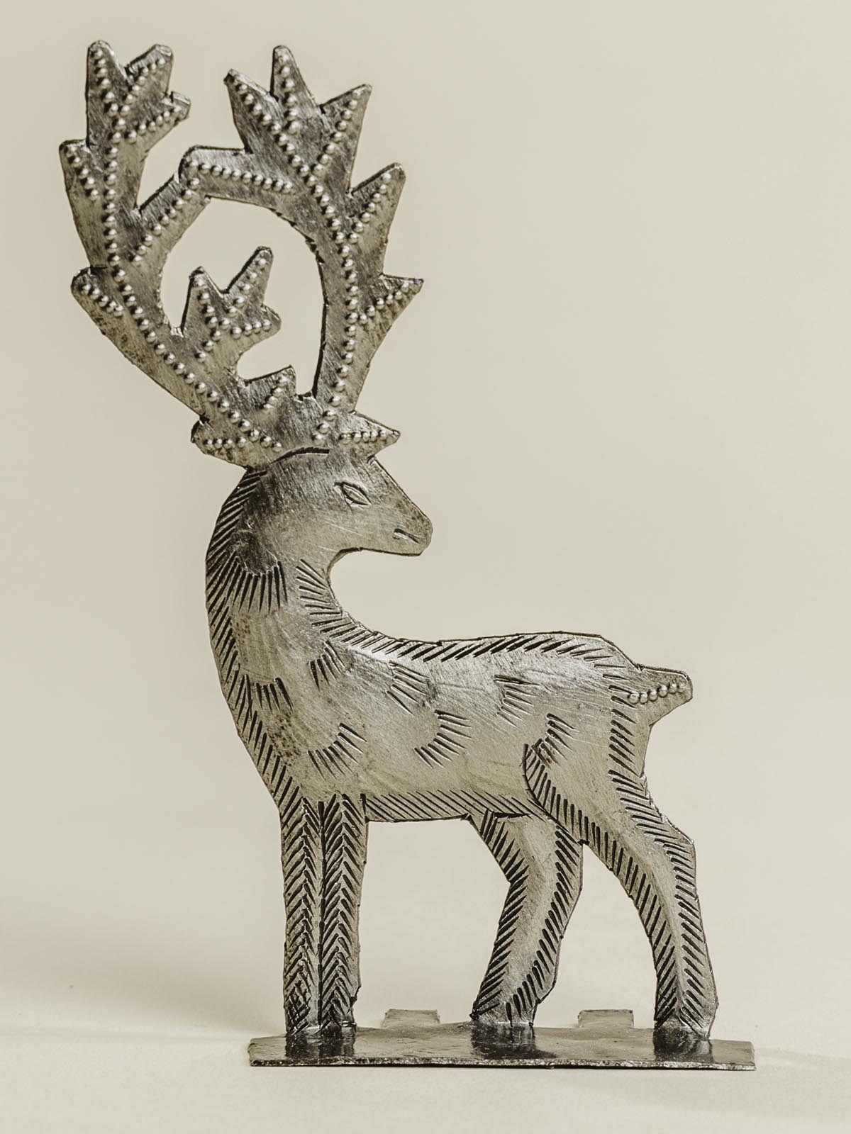 Silver metal reindeer standing on a beige background. 