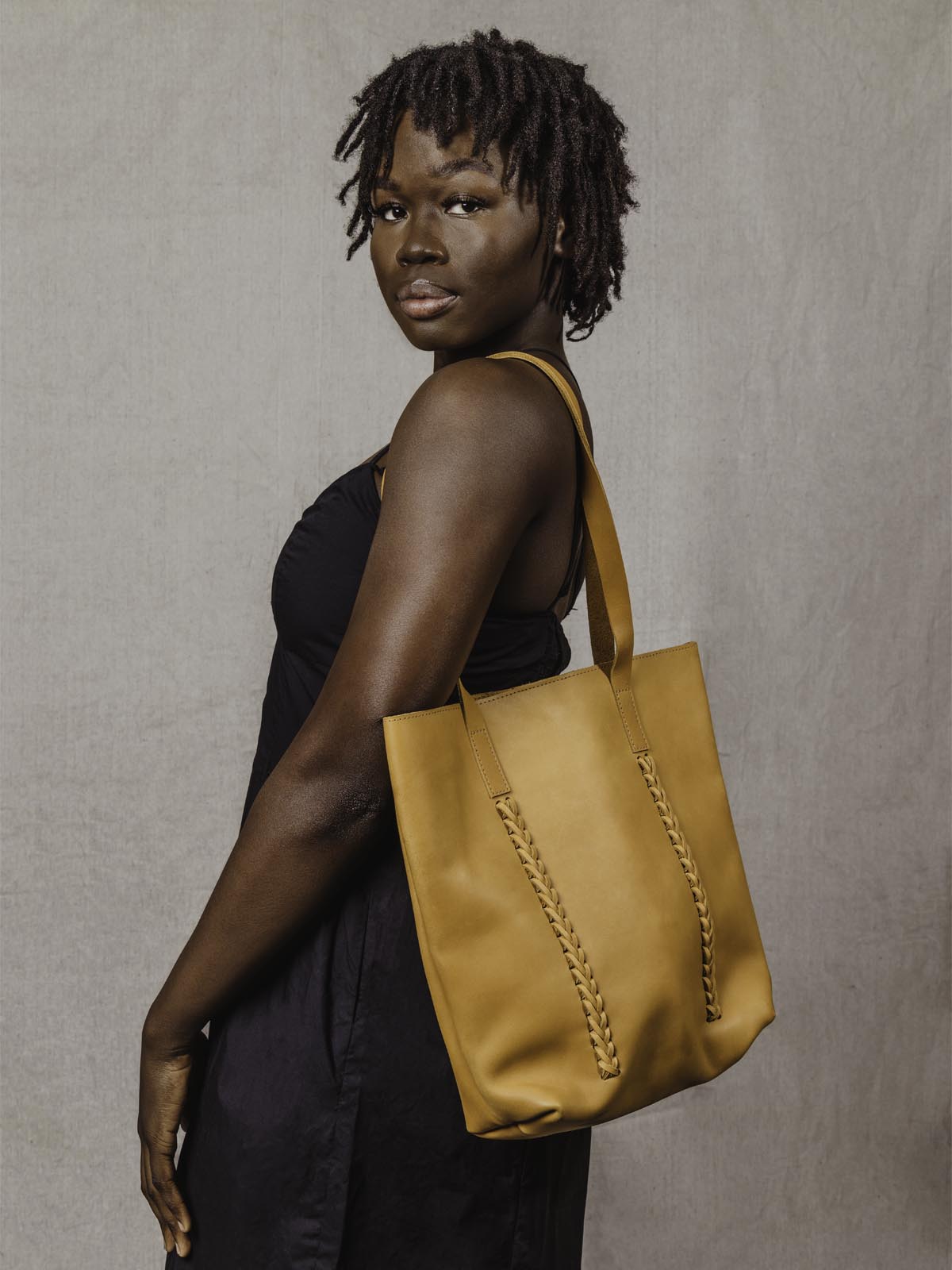 Model with tote back over shoulder in a black dress.