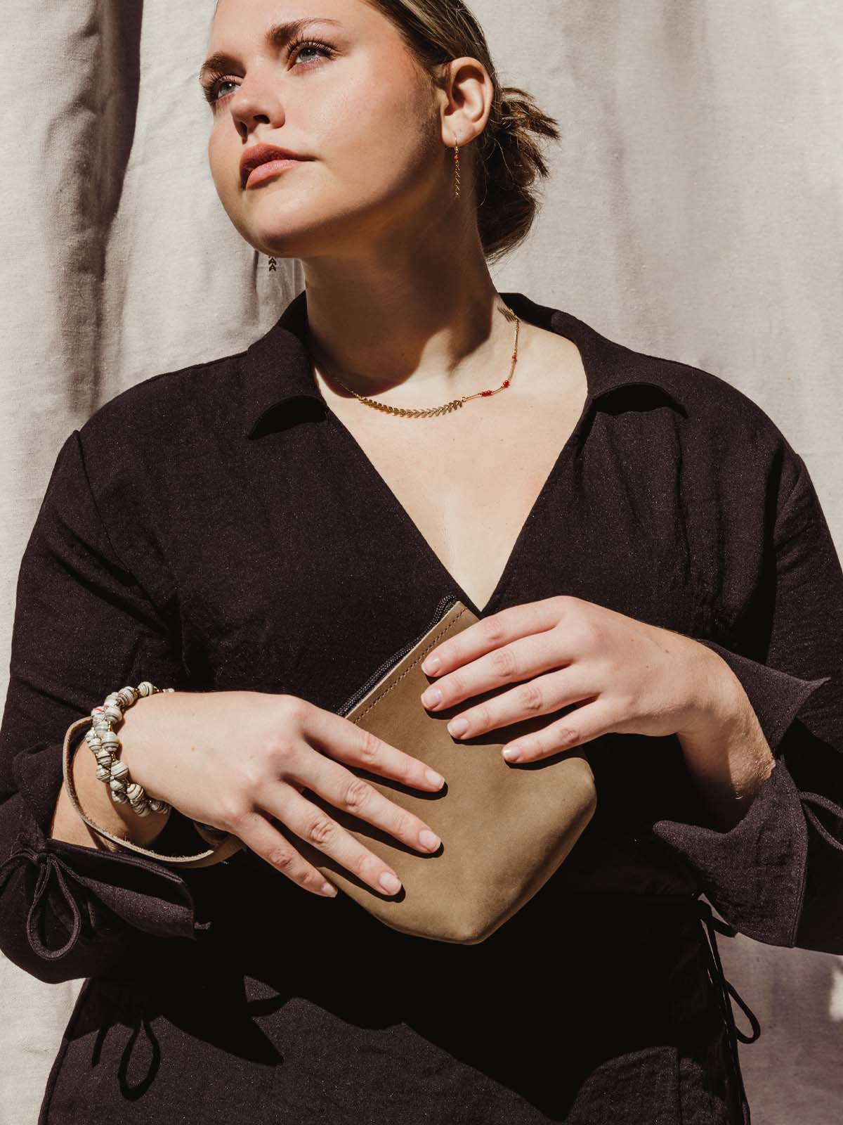 female model holding brown leather wristlet 